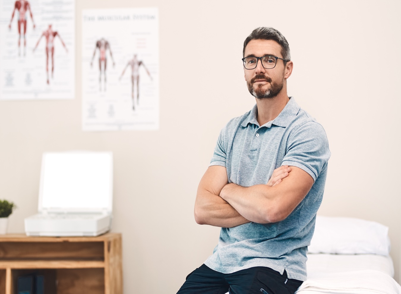 A man in casual dress sits in a doctor’s office with a neutral expression, waiting for an appointment, representing the importance of comprehensive employee benefits such as healthcare.