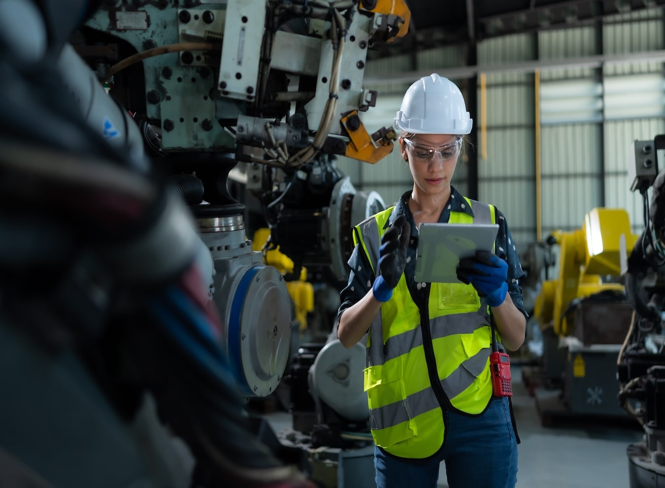 A woman in training at a warehouse uses an iPad to take an assessment while facing an industrial robot, highlighting the integration of technology and robotics in the modern industrial workplace.