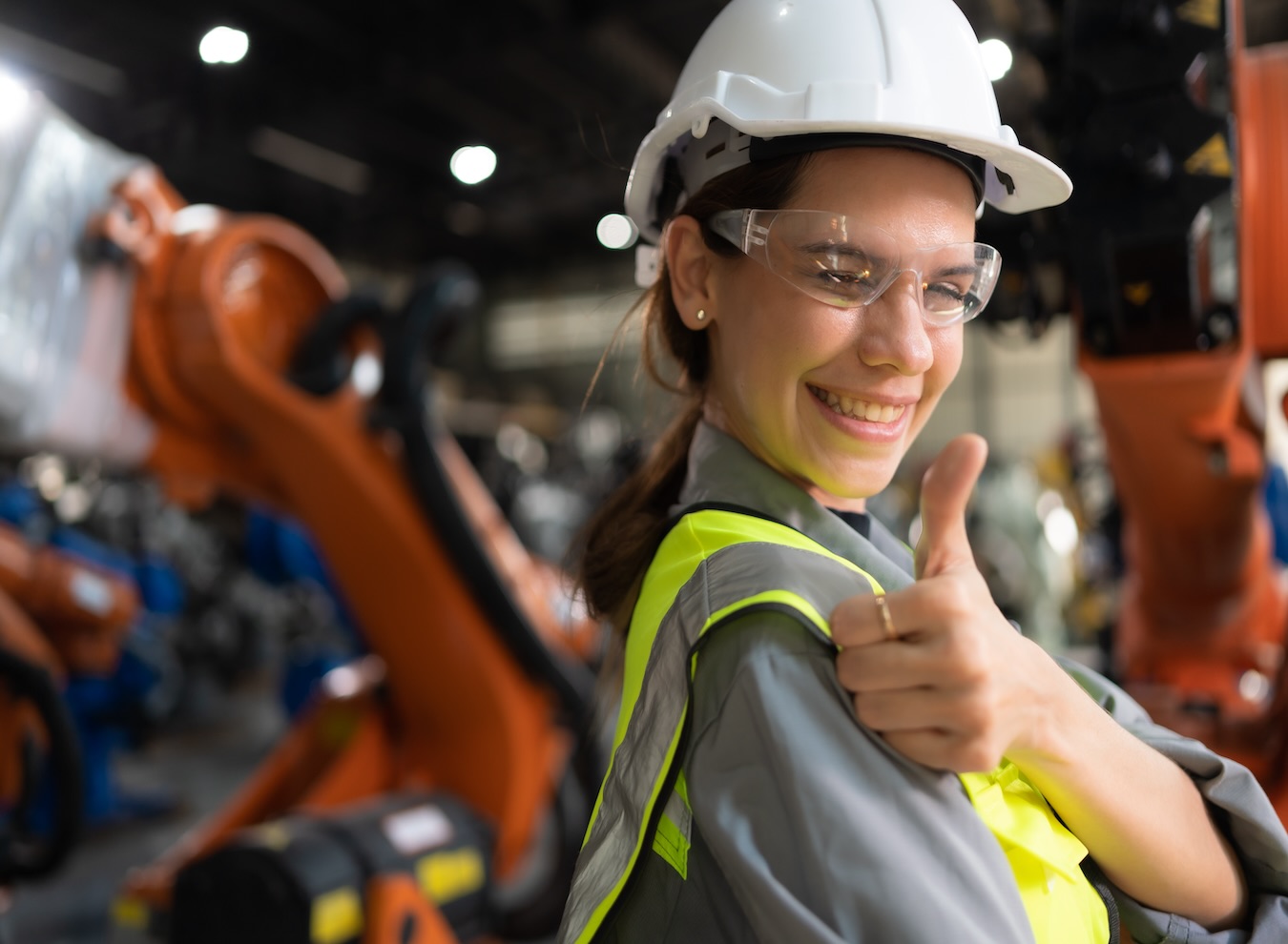 A happy woman in a factory gives a thumbs up, representing high morale and a positive company culture in an industrial workplace.